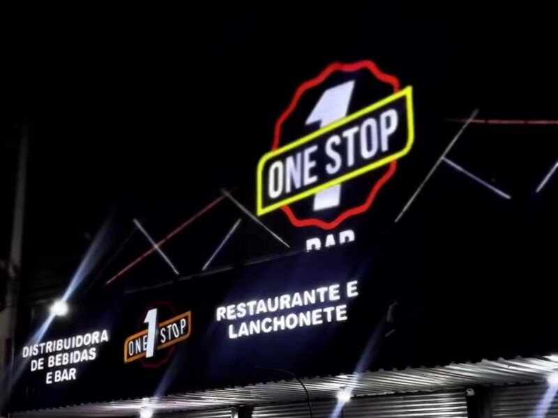 Fachada do One Stop Bar à noite, com o letreiro iluminado