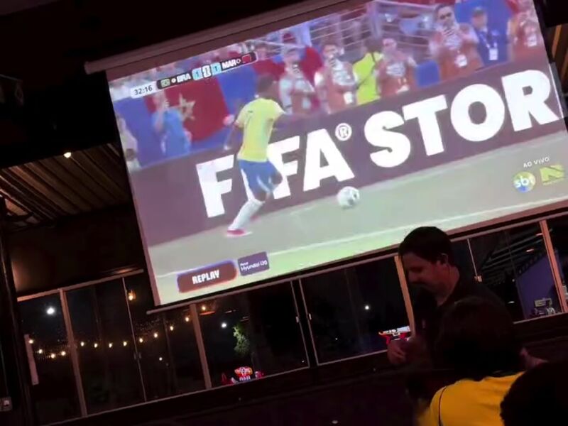 Telão transmitindo jogo de futebol para as mesas